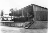 Vägstation G. Okänd plats. Lastbrygga med öppet förråd bakom, upplag av slangar, sprängmattor m. m.