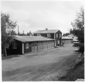 Vägstation G4, Bergsnäs. Byggnad med mittdel i två våningar, troligtvis kontorsdel, flankerade av två längor garage. Längst till vänster eventuell verkstadsdel. Spetsplogar i fonden. Invid väg.