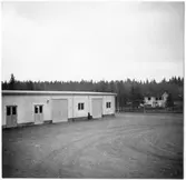 Vägstation G10, Åseda. Förrådsbyggnad, bostadshus i bakgrunden.