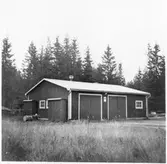 Vägstation G10, Åseda. Filial Braås. Förråds- och garagebyggnad. Vid gaveln manskapsskåp för manskapets personliga utrustning och redskap. Slipstenbock med slipsten. Bränslefat.