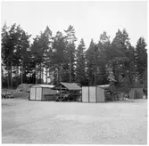 Vägstation H4, Hjorted. Garageplan med olika små förrådsbyggnader, materielupplag, cementrör, bränslefat.