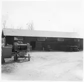 Vägstation H5, Vimmerby. Förrådsbyggnad. Upplag av bränslefat. Stenkross i förgrunden.