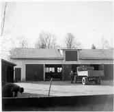 Vägstation H5, Vimmerby. Verkstadsbyggnad. På garageplan lastbil H7474, med mansperson vid förarhytten. En port till verkstaden öppen. Mansperson i förgrunden.