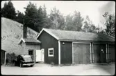 Vägstation H7, Högsby.  Förråds- och garagebyggnader. Personbil Mercedes vid gaveln.