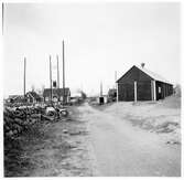 Vägstation H11, Borgholm, filial Högby. Garage- och förrådsbyggnad. Invid väg med stenmur. Bostadshus på andra sidan vägen.