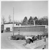 Vägstation L3, Örkelljunga. Garageplan på vägstationen. I fonden garage- och förrådsbyggnader. I förgrunden bränslefat framför lastbrygga. Personbilar.