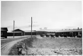 Vägstation L5, Broby. Vy från väg mot vägstationen, med garagebyggnad, med spetsplogar framför.