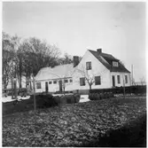 Vägstation M4, Beddinge. Bostadshus, troligen inrymmande kontor sammankopplat med förrådsbyggnad. Bensinpump (drivmedelspump) framför, personbil framför förrådsbyggnaden.