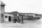 Vägstation N4, Vinberg. Garageplan framför garagebyggnad. Bensinpumpar (drivmedelspumpar), varav en av märket Ljungmans, modell Vici. En mansperson vid pumpen. I bakgrunden smörjbrygga och upplag av cementrör. Luttunna.