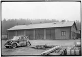 Vägstation O6, Naverstad. Garagebyggnad. På garageplan personbil O11376, vägsladd. Upplag av bränslefat.