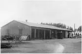 Vägstation P2, Kinna. Garagebyggnad med smedja i bortre änden. Framför byggnaden torrdass och personbil.