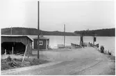 Vägstation P16, Bengtsfors. Färjeläget Jaren. Färjeläget med väntkur, förrådsbyggnad. Färja 61/32 ligger vid kajen, betongfärja byggd 1939, i trafik till c:a 1965. En personbil på färjan. Manspersoner invid färjan.