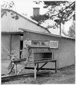 Vägstation R13, Skövde. Förrådsbyggnad och del av garagebyggnaden. Moped lutad mot bord med odefinierat verktyg, eventuellt plåtsax.