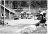 Vägstation S5, Sysslebäck. Vy över vägstationen med garage- och förrådsbyggnader. I fonden bostadshus. Liten lastbil (paketbil) och personbil på garageplan.