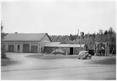 Vägstation S9 Kil. Garagebyggnad och förrådsbyggnader. Bensinpump (drivmedelspump), två personbilar. Luttunna till höger. Invid väg.