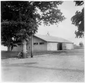 Vägstation T3, Hallsberg. Förrådsbyggnad. Cykel lutad mot ett träd.