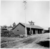 Vägstation T7, Frövi.  Förrådsbyggnad, eventuellt äldre garagebyggnad. Bensinpumpar (drivmedelspumpar) framför byggnaden, varav en Ljungmans, modell Vici. Järnväg (bangård) i bakgrunden.