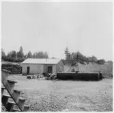 Vägstation T8, Grythyttan. Vägstationens grusgrop med förrådsbyggnad, två oljecisterner, upplag av bränslefat.