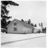 Vägstation U4, Salbohed. Förrådsbyggnad. I bakgrunden garagebyggnad och olika förrådsbyggnader. Bensinpump (drivmedelspump). Transportband framför garagebyggnad i bakgrunden. Invid väg.