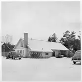 Vägstation U4, Salbohed. Garagebyggnad (baksidan). Verkstad och smedja till vänster. Cykelställ med cyklar, två personbilar, bland annat U8485. Förrådsbyggnad och bensinpump (drivmedelspump) i bakgrunden.