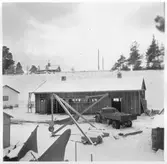 Vägstation U5, Heby. Förrådsbyggnad. På garageplan lastbil, mansperson bredvid lastbilen. Sidoplogar. Vinsch med handdrivet wirespel. Cyklar.