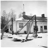 Vägstation U6, Anundshög. Garagebyggnad (baksidan). Troligtvis verkstadsdel och smedja i byggnadens vänstra del. Sten- och stubbrytare i förgrunden. Spetsplog vid byggnadens framsida.