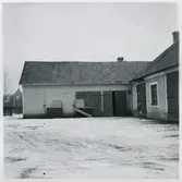 Vägstation U7, Kolbäck. Förrådsbyggnad, hopbyggd i vinkel med verkstads- garagebyggnaden. Bostadshus i bakgrunden. Cykel utanför verkstaden.