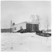 Vägstation U8, Fjärdhundra, filial Tärna. Garagebyggnad. Spetsplog och cyklar vid väggen. Framför byggnaden vägsladd, modell Arbrå.