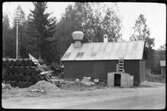 Vägstation W 6, Falun, filial Bjursås. Garagebyggnad. Upplag av bränslefat, vägmärken lutade mot faten. Invid väg.