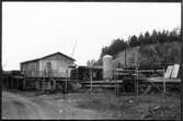 Vägstation W 6, Falun, filial Bäckehagen. Förrådsbyggnad, upplag av diverse material, innanför nätstängsel.