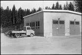 Vägstation Vmo X6, Forsa. Verkstadsbyggnad. Paketbil (liten lastbil) och personbilar. Garagebyggnad i bakgrunden.