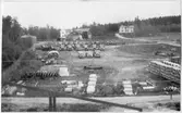 Vägstation Y6, Älandsbro. Uppställning av lastbilar och personbilar, förmodligen med koppling till depåverkstaden. Husvagn till vänster. I förgrunden upplag av cementrör. Bondgård och bostadshus i bakgrunden.