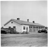 Vägstation Y12, Sollefteå. Vägstationens huvudbyggnad med kontor och garage. På bänk framför byggnaden två barn. Personbil på garageplan. Vid gaveln upplag av fasta snöskärmar, så kallade flakskärmar. Cyklar och vedupplag vid gaveln.