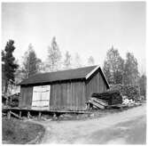 Vägstation Y14, Ramsele. Förrådsbyggnad med lastramp. Upplag av ved och bränslefat. Vid gaveln hoprullade snöskärmar (kättingsnöskärm), liten släde (kälke) av trä.