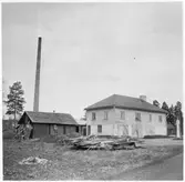 Vägstation Y16, Hoting. Garage- och kontorsbyggnad. Förrådsbyggnad i bakgrunden. Bensinpump (drivmedelspump). Vägmärken lutade mot förrådsbyggnaden. Hög industriskorsten i bakgrunden. Invid väg.