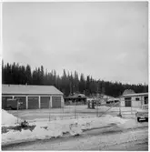 Vägstation Z13, Gäddede. Till vänster vägstationens huvudbyggnad med garagedelen. Förrådsbyggnad till höger och i bakgrunden. På garageplan bensinpumpar (drivmedelspumpar). Manskapsvagn till vänster. Nätstängsel och grind runt anläggningen. Utanför grinden personbil Opel Z13276. Bostadshus i bakgrunden. Invid väg. (Vinterbild).