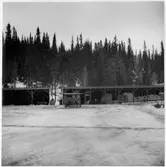 Vägstation Z13, Gäddede. Förrådsbyggnad, öppna skjul, med virkesupplag. (Vinterbild).