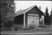 Vägstation AC12, Norsjö. Garage- och förrådsbyggnad. Förråd i byggnadens bakre del. Affischer på väggen, eventuellt valaffischer. Invid väg.