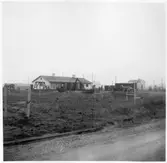 Vägstation BD2, Älvsbyn. Vy mot vägstationen med garage- och kontorsbyggnaden i bakgrunden. Förrådsbyggnad till höger. Luttunna, sidoplog, lastbil personbil framför byggnaderna. Invid väg.