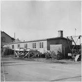 Vägstation BD4 Boden, Svartbjörnsbyn. Förrådsbyggnad. Eventuellt verkstad (smedja) i byggnadens främre del. Bostadshus i bakgrunden. Sandspridare, wirevinsch, lastbrygga. Invid väg.