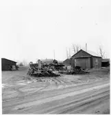 Vägstation BD6, Råneå. Förrådsbyggnad, till vänster. Mot byggnaden upprest sandspridare. Byggnad, eventuellt manskapsbod, till höger. Upplag av olika väghållningsmaskiner, bland annat vägsladdar. Cyklar, bensinpump (drivmedelspump). Bostadshus i bakgrunden. Invid väg.