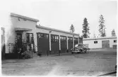 Vägstation BD12, Korpilombolo. Vägstationens huvudbyggnad med verkstad, kontor och garage. Personbil på garageplan. Förrådsbyggnad i bakgrunden.