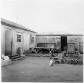 Kvarteret Stören, Luleå. Förrådsbyggnader. Upplag av diverse materiel framför byggnaderna. Eventuellt kompressor. Cykel.