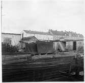 Kvarteret Stören, Luleå. Förrådsbyggnader. Upplag av diverse materiel. I bakgrunden bostadshus, bland bostadshuset (till vänster) Bostadsrättsföreningen Sillen, uppförd 1939.