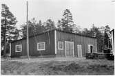 Byggnadsförrådet i VFBD (Vägstation VFBD7, Kalix). Förrådsbyggnad. Framför byggnaden redskapslådor.