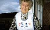 Stina Svensson (1912 - 2001) iklädd förkläde, står på entrétrappan till Hembygdsgården Långåker 1:3, 1980-tal.