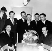 Sju män samlade runt ett bord. På bordet står en korg som skall lottas ut. 

Sittande till vänster om bordet: Gunnar 