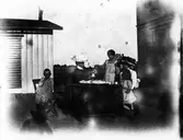 Gruppbild. Två kvinnor, två flickor och en pojke vid ett dukat bord i en trädgård.