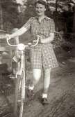 Ingrid Andersson (1918 - 2001, gift Skansing) står med en cykel ute i naturen, Livered 