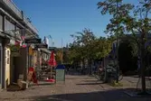 Almåsgången i riktning mot öster. Lindome centrum den 4 oktober 2016. Till vänster ses huset Almåsgången 2 som inrymmer en del affärer, närmast ses Lindome Spel & Tobak, Lindomefloristerna samt ICA Supermarket. Till höger huset Almåsgången 1. I fonden ses även Lindome kyrka.